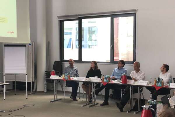 Menschen an Tischen hören der Präsentation zu.