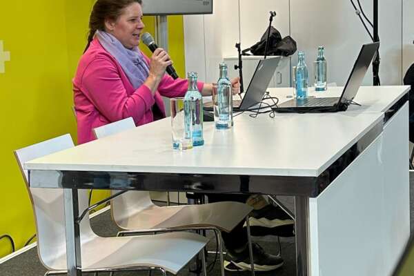 Eine Frau sitzt an einem Tisch und hält einen Vortrag mit Präsentation.