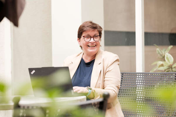 Frau sitzt mit Laptop draußen im Grünen.