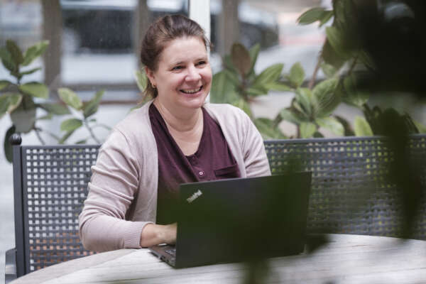 Frau sitzt draußen an einem Tisch mit einem Laptop.