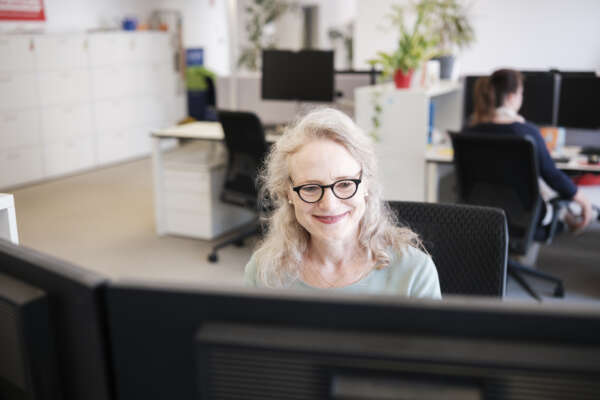 Eine lächelnde Frau sitzt an einem Schreibtisch.