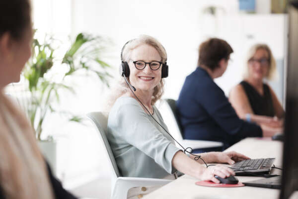 Frau sitzt mit Headset am Computer im Coworking Space.