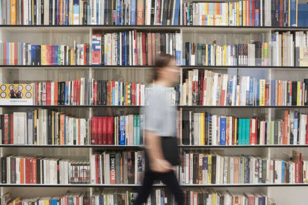 Eine verschwommene Person geht vor einem Bücherregal her.
