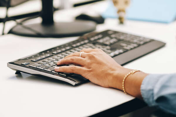 Person sitzt an Schreibtisch mit einer Hand auf der Tastatur.