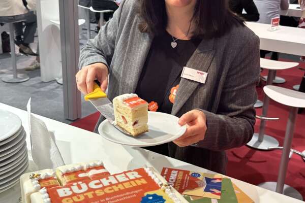Eine Frau schneidet die büchergutschein-Torte an und lächelt in die Kamera.