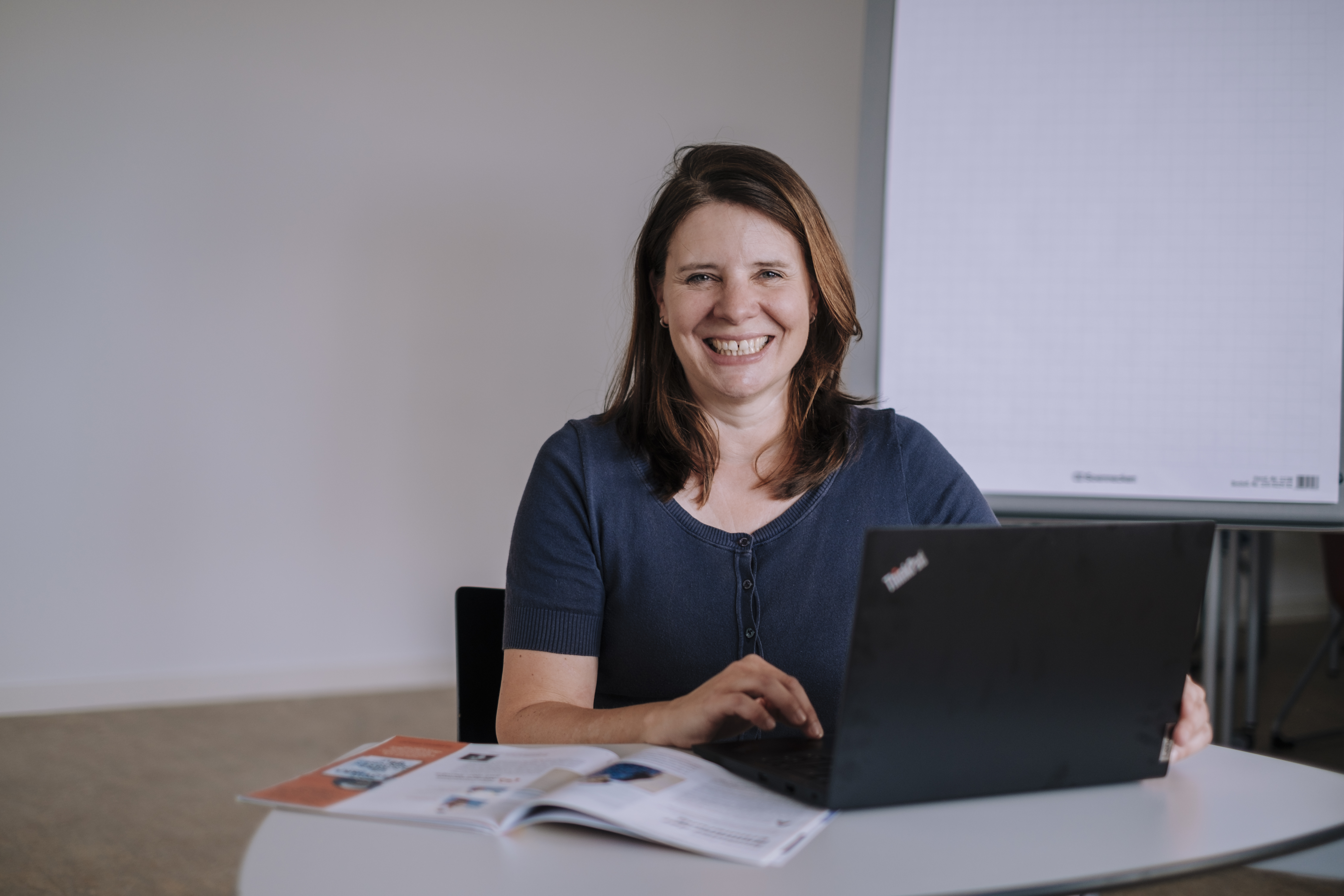 Frau sitzt am Laptop und lächelt in die Kamera.