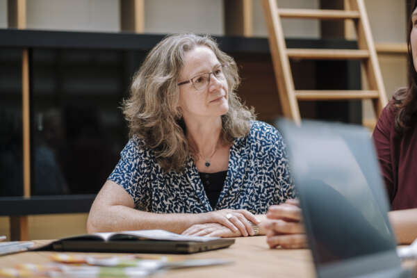 Frau sitzt an einem Tisch und unterhält sich mit jemandem außerhalb des Fotos.