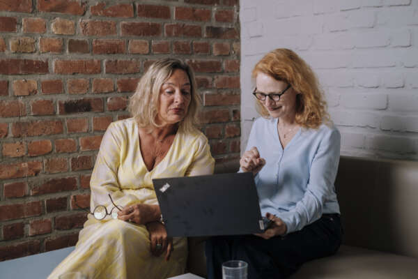Zwei Frauen sitzen zusammen und schauen auf einen Laptop.