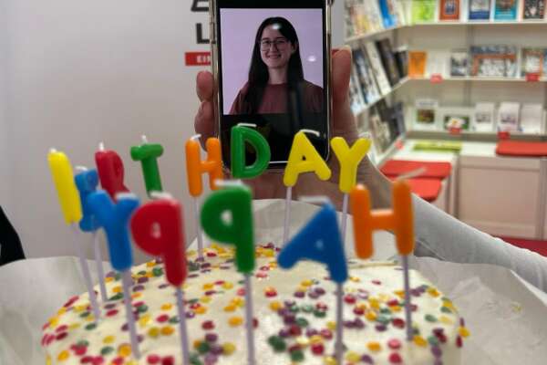 Hinter einem Kuchen mit Happy Birthday Kerzen sieht man ein Bild von Franziska Werum auf einem Handy.