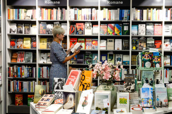 Frau mit offenem Buch in der Hand vor einem Bücherregal in einer Buchhandlung.